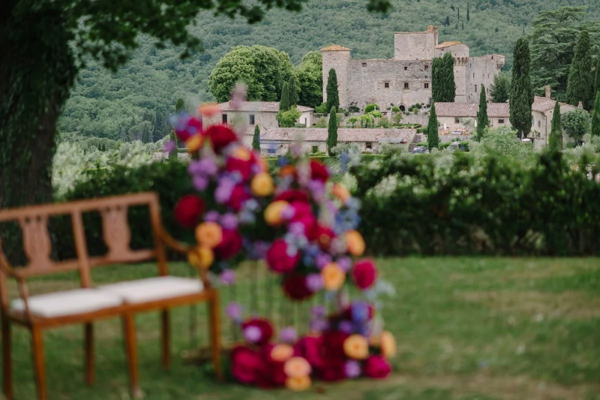 Close-up of the wedding ceremony chairs with floral details at Castello di Meleto, with the historic castle softly visible in the background in Tuscany.