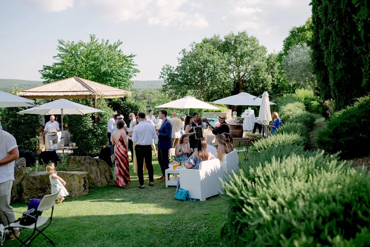 Guests mingling during aperitivo in the garden at Casa Cornacchi, with open umbrellas and relaxed outdoor atmosphere in Tuscany