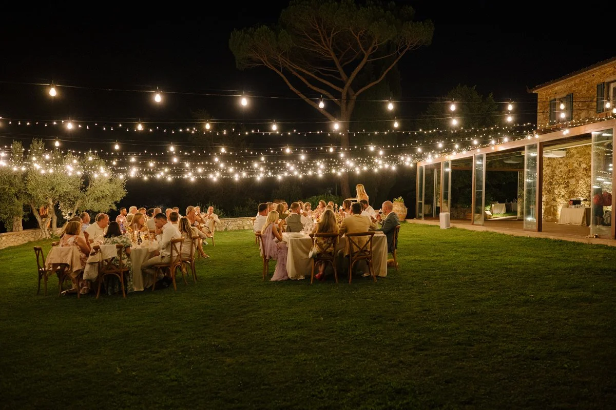 Wedding dinner with guests seated outdoors under string lights at Le Filigare wedding venue in Tuscan