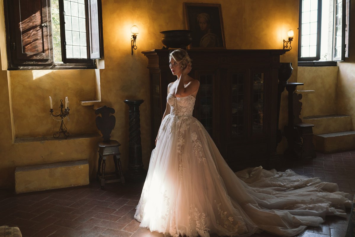 Bride in her wedding dress looking at herself in the mirror inside one of the historic rooms at Castello Il Palagio.