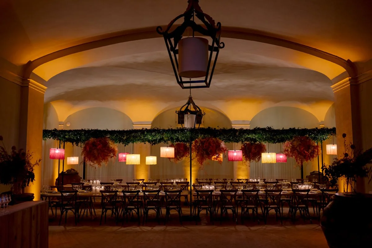 Indoor welcome dinner at Torre a Cona with colorful chandeliers and floral installations above long tables.