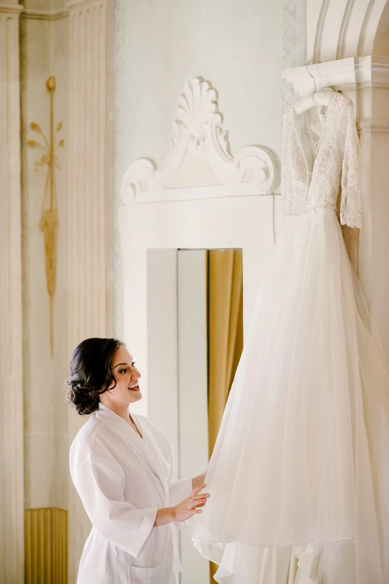 Bride looking at her wedding dress hanging inside a room at Villa Hotel Tolomei wedding venue.