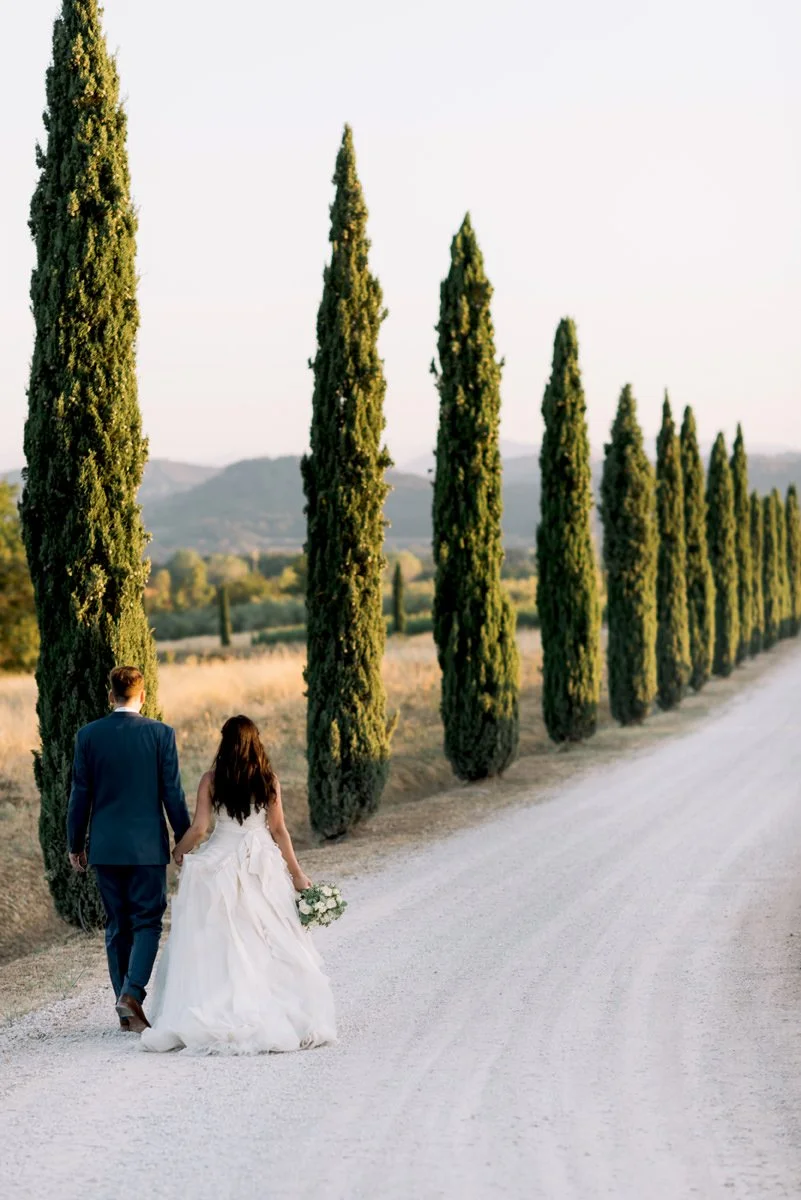 Wedding couple walking along a cypress-lined road at Conti di San Bonifacio in Tuscany.