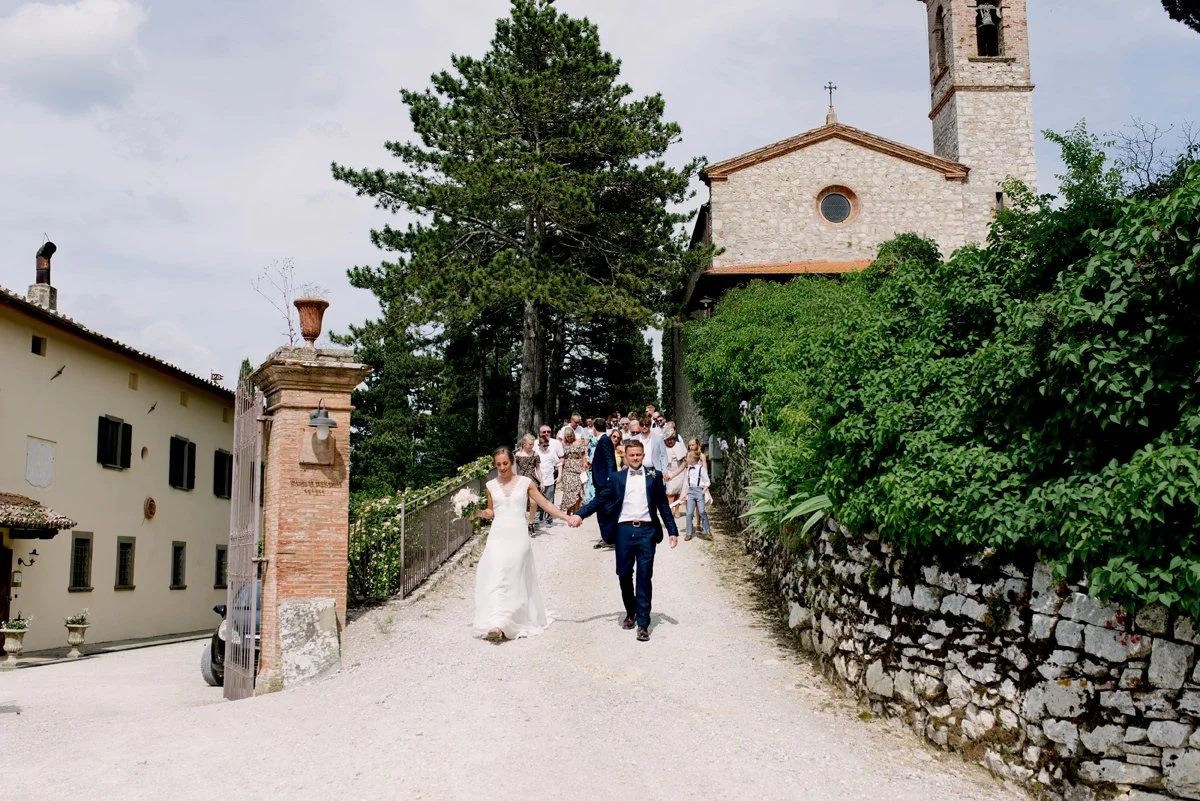 Bride, groom, and wedding guests walking together toward aperitivo at Borgo Pietrafitta.