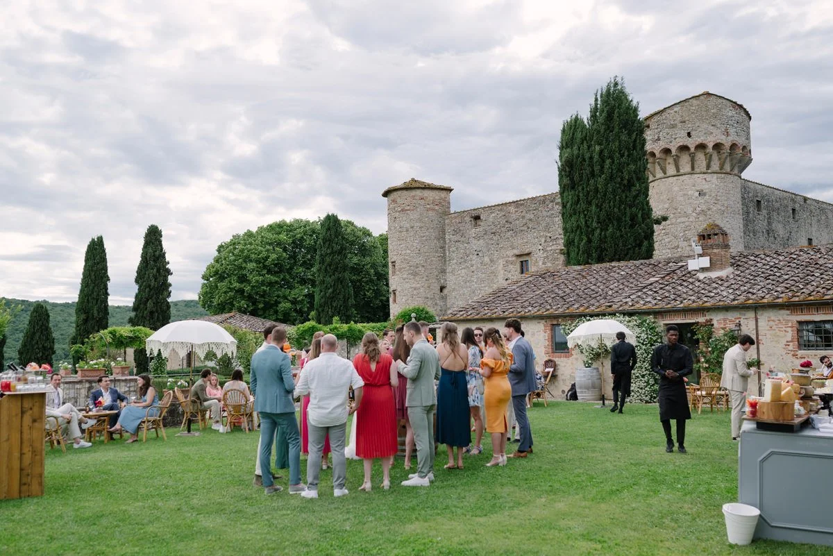 Wedding aperitivo in the Italian garden at Castello di Meleto, with guests gathered among greenery and the castle forming the backdrop in Tuscany.