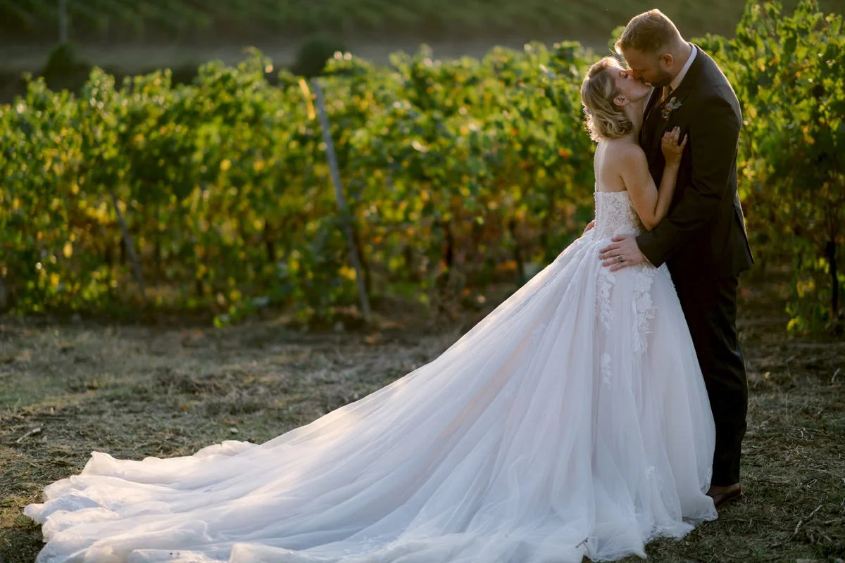 Bride and groom kissing among the vineyards surrounding Castello Il Palagio in Tuscany.