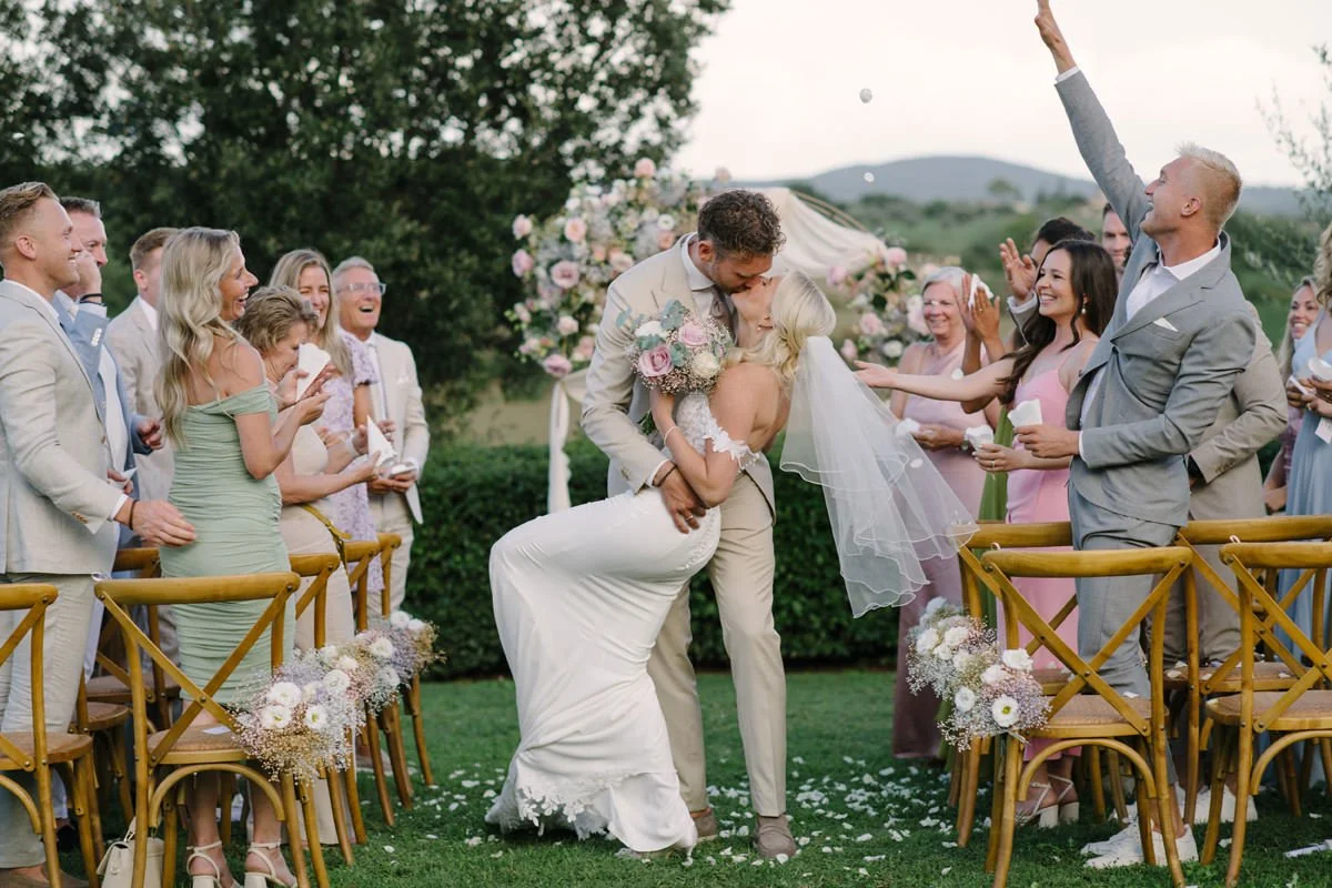 Bride and groom kissing at the end of their ceremony while walking between rows of guests at Villa Boscarello.