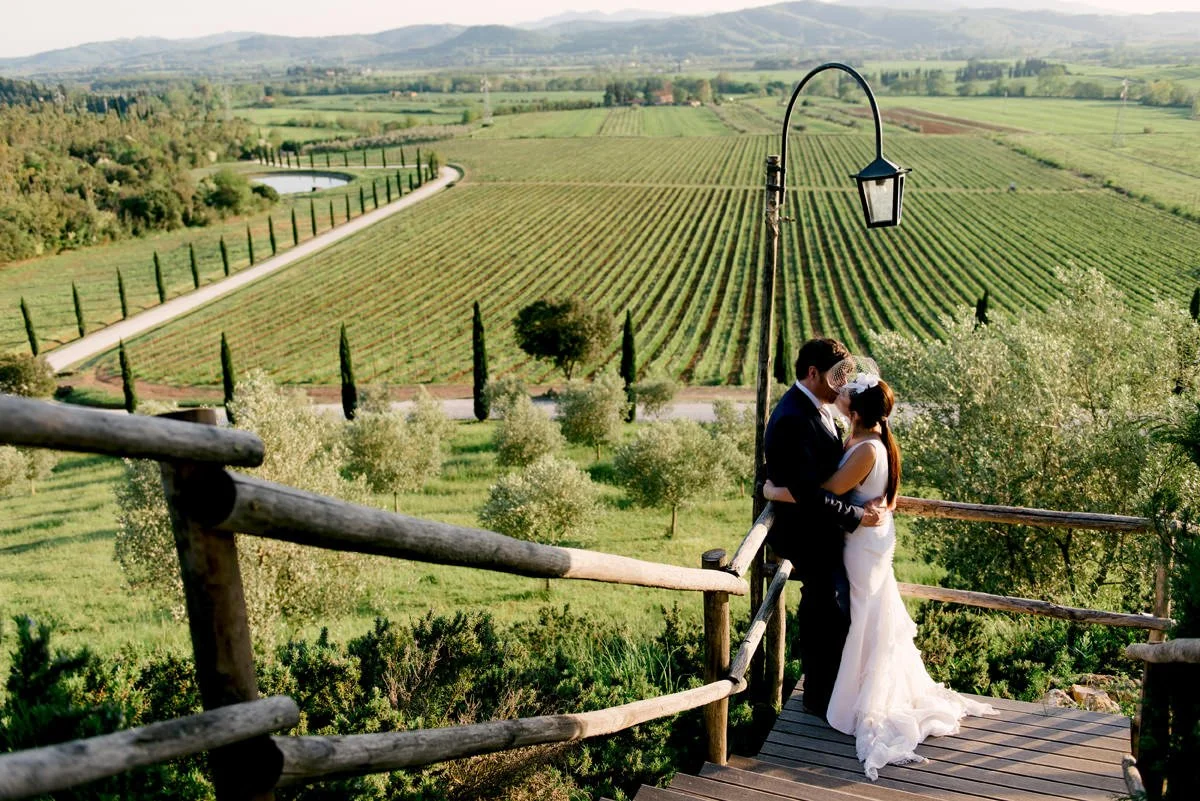 Wedding couple standing close together on the stairs with vineyards in the background at Conti di San Bonifacio.