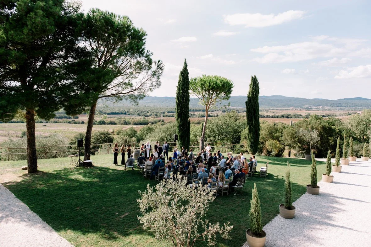 Wedding ceremony at Conti di San Bonifacio set beside large trees with Tuscan countryside views.