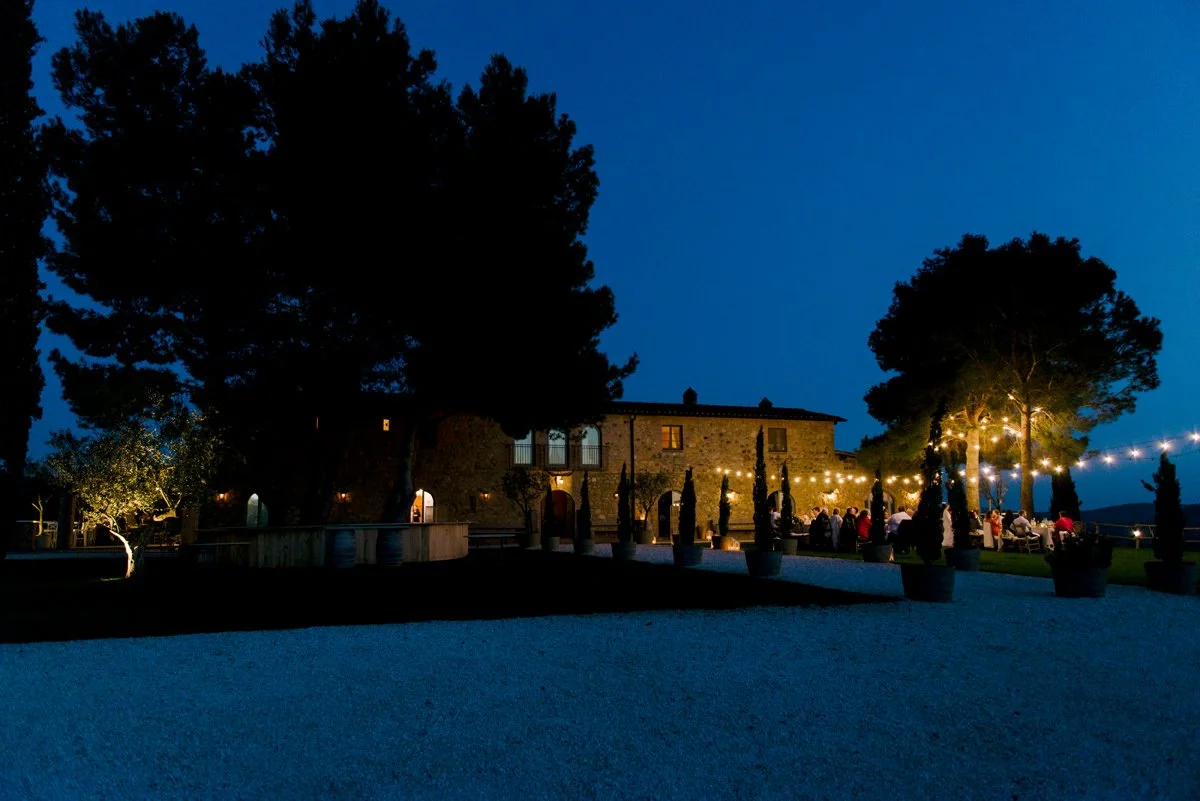 Outdoor wedding dinner with string lights set in front of Conti di San Bonifacio wine estate in Tuscany.