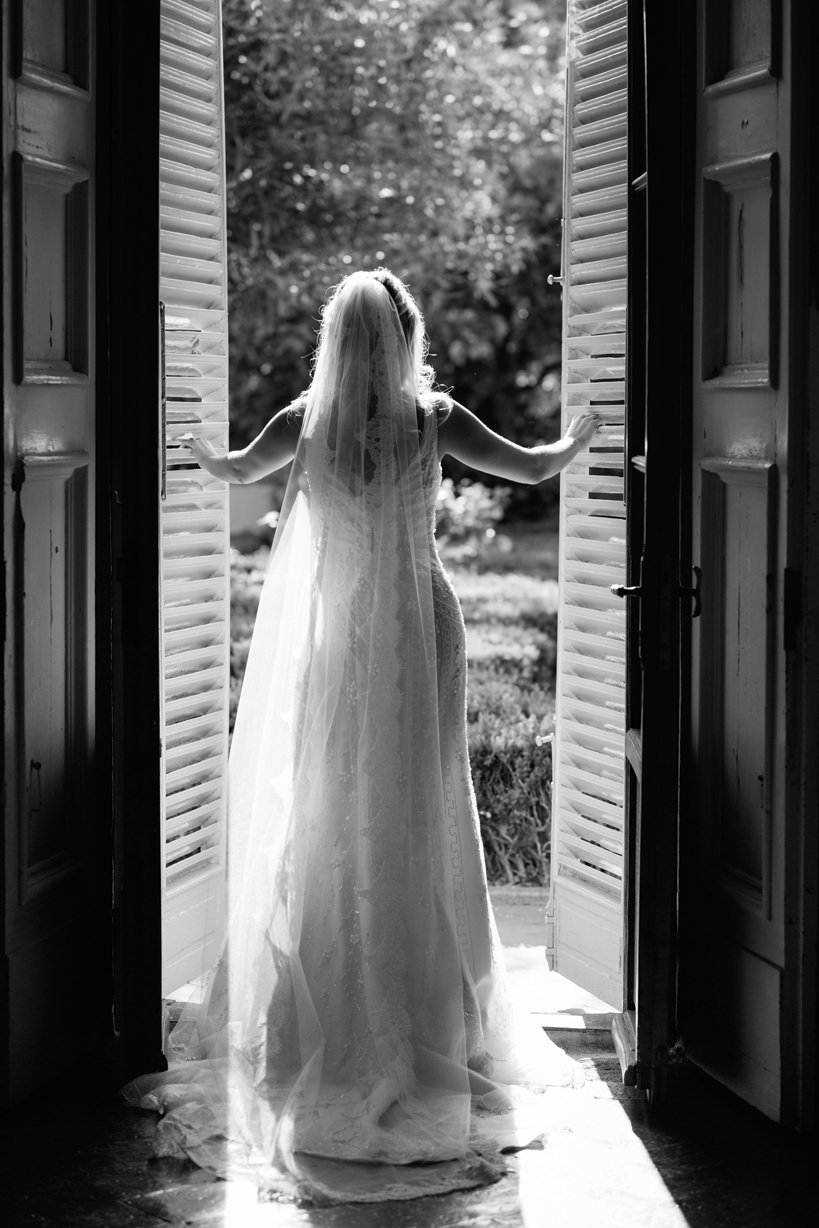 Black and white fine-art portrait of the bride opening the door inside Castello di Montegufoni before the wedding ceremony.
