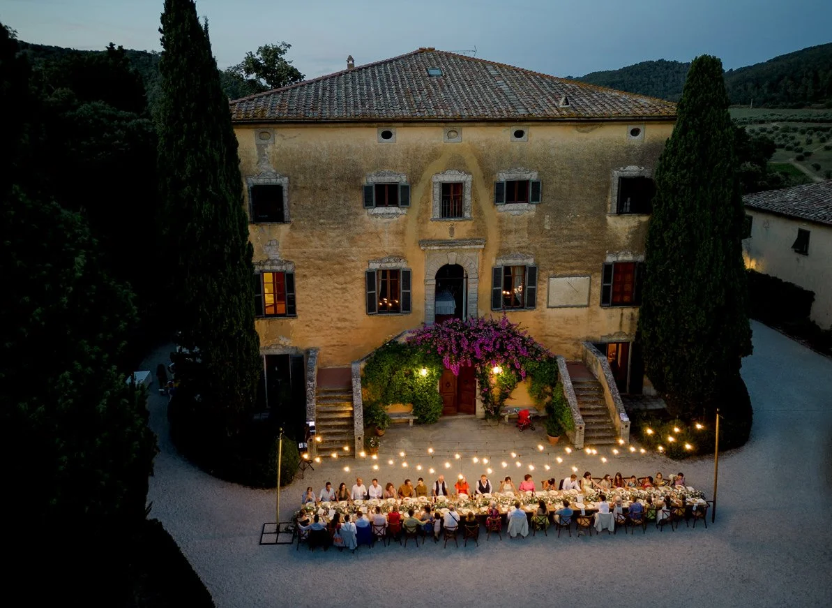 Wedding dinner at Villa di Ulignano with string lights illuminating long tables set in front of the villa façade.