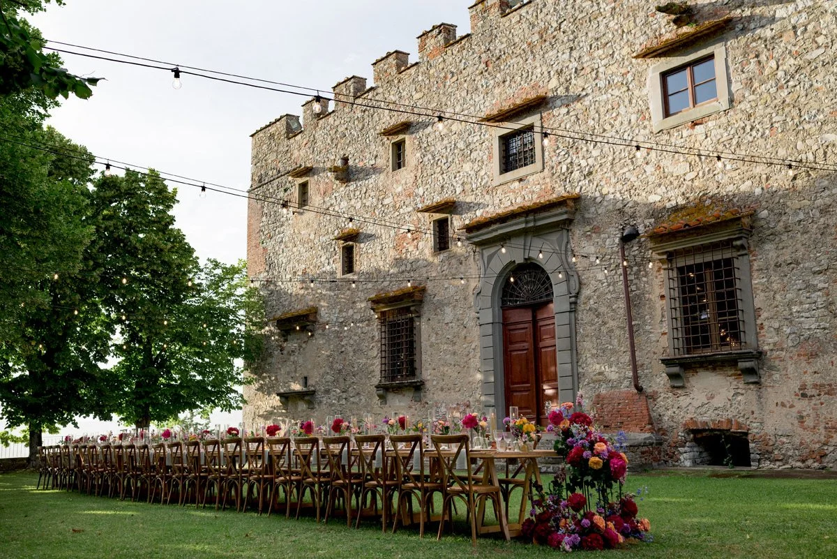 Wedding dinner in the courtyard of Castello di Meleto, with floral styling and the castle as the backdrop.