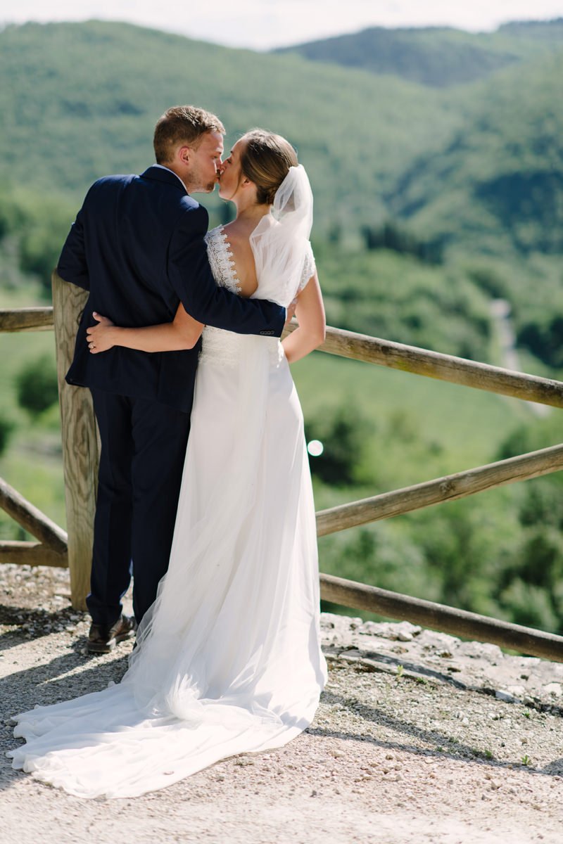 Bride and groom kissing on a terrace at Borgo Pietrafitta with panoramic views of the Tuscan landscape.