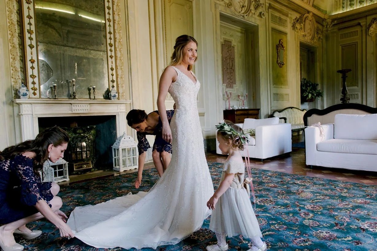 Bride smiling with her flower girl in a large historic room at Castello di Montegufoni during wedding preparations.