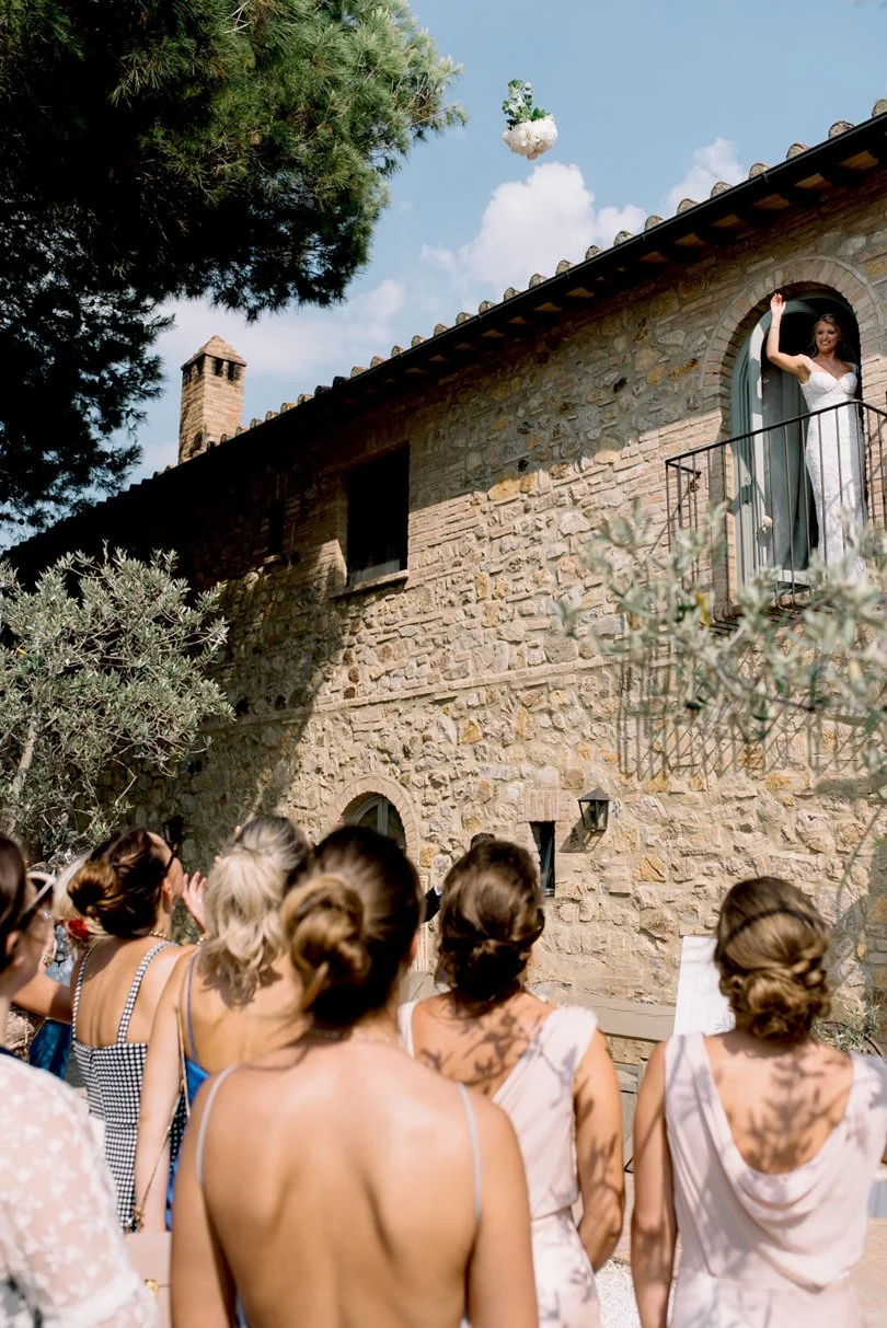 Bride throwing her bouquet through a window while guests wait below at Conti di San Bonifacio.
