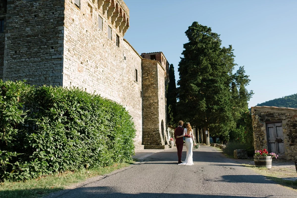 Bride and groom walking in front of the fortified exterior walls of Castello del Trebbio in Tuscany.