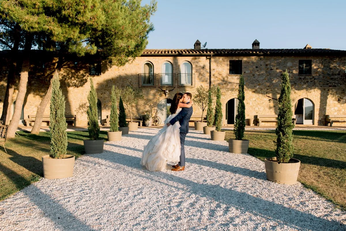 Wedding couple kissing in front of Conti di San Bonifacio wine estate in Tuscany, with the historic property and countryside atmosphere behind them.