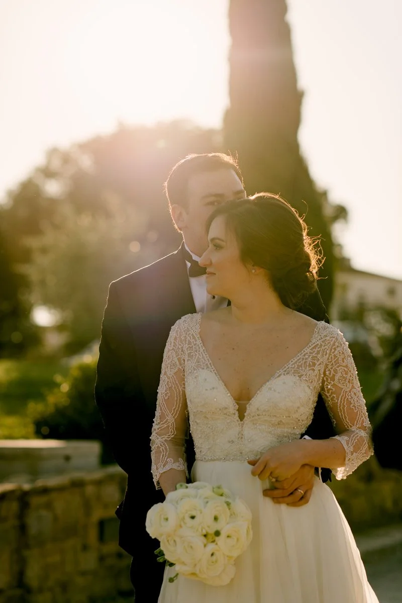 Bride and groom kissing at sunset on the terrace of Villa Hotel Tolomei with Tuscan hills behind.