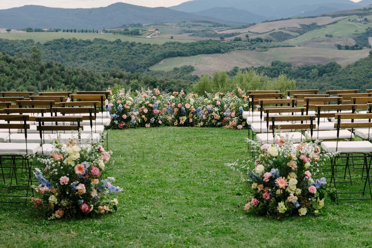 Wide view of the meadow-style ceremony floral wall facing the Tuscan countryside at Villa di Ulignano