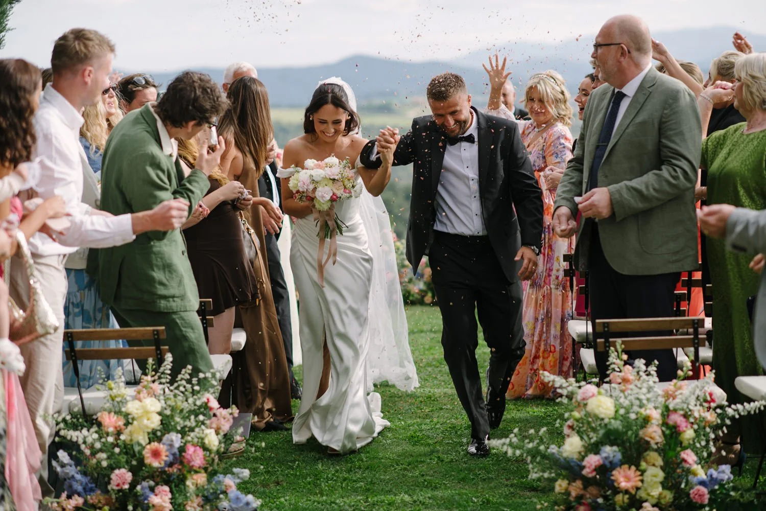 Bride and groom recessional with raised hands as guests throw petals at Villa di Ulignano, FunkyBird