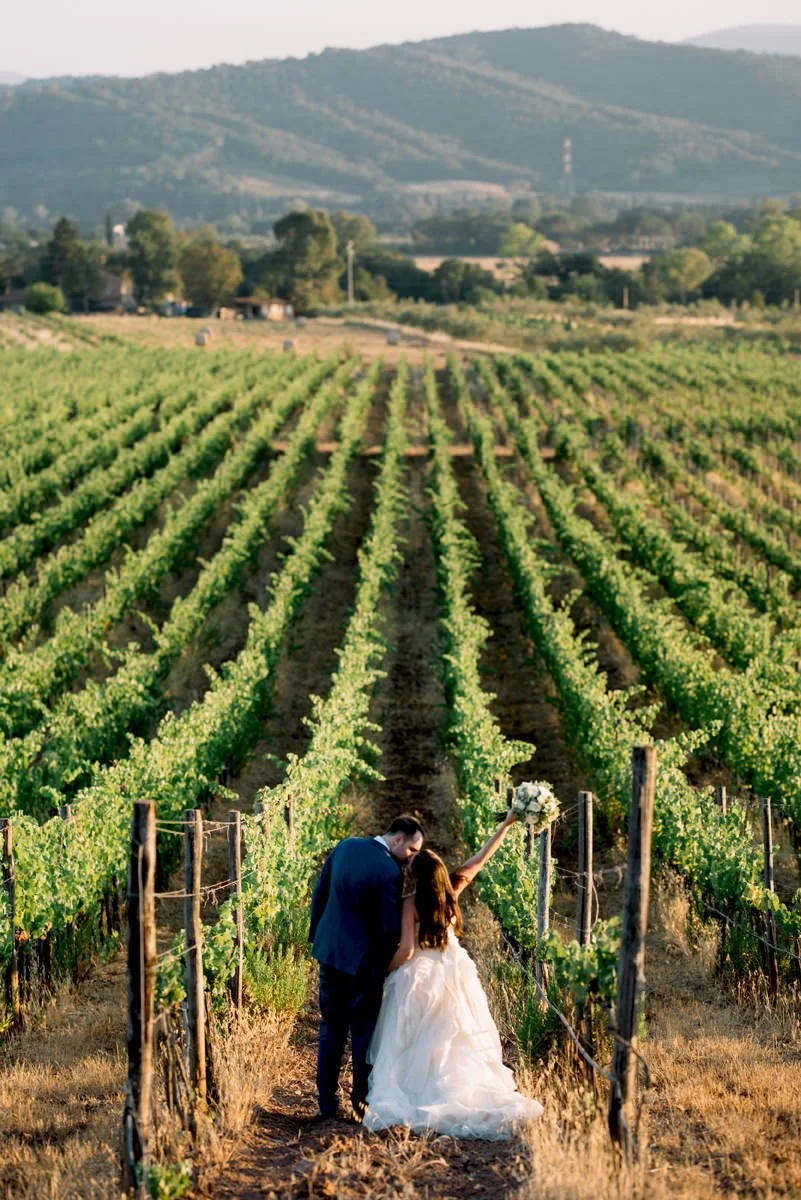 Wedding couple kissing in the vineyards at Conti di San Bonifacio wine estate in Tuscany during golden hour.