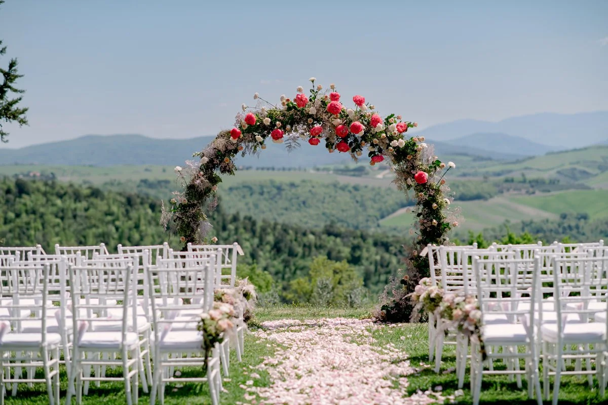 Round floral ceremony arch by FunkyBird Weddings set at the poolside ceremony spot at Villa di Ulignano with open landscape views.