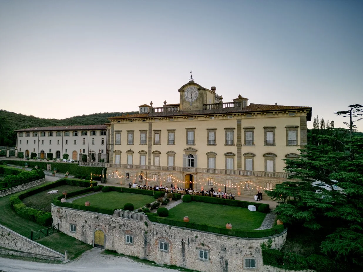 Wide view of a wedding dinner table in front of Torre a Cona villa with string lights overhead in Tuscany.