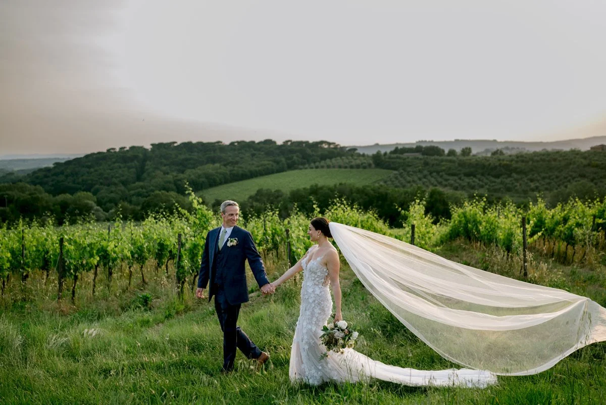Bride and groom walking together in front of the vineyards at Castello di Bossi during their Tuscany wedding.