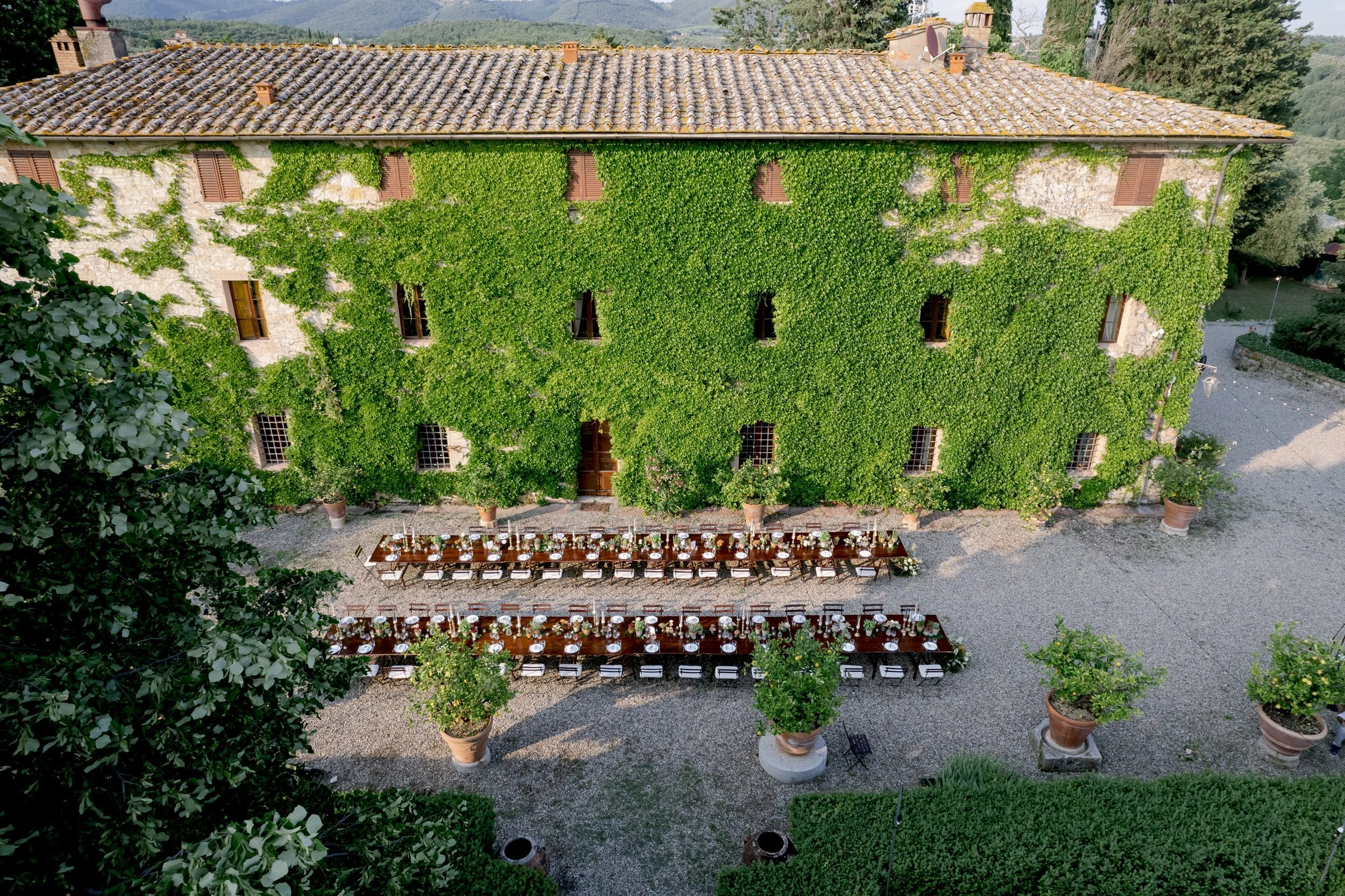 Long wedding dinner tables set in front of Castello di Bossi, with historic stone walls covered in green ivy.