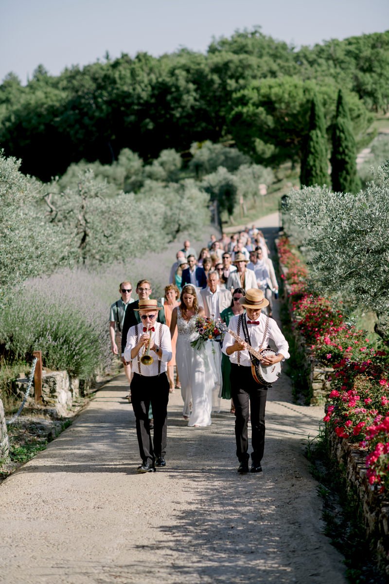 Wedding guests walking back from the ceremony while two musicians play music in front of them at Le Filigare.
