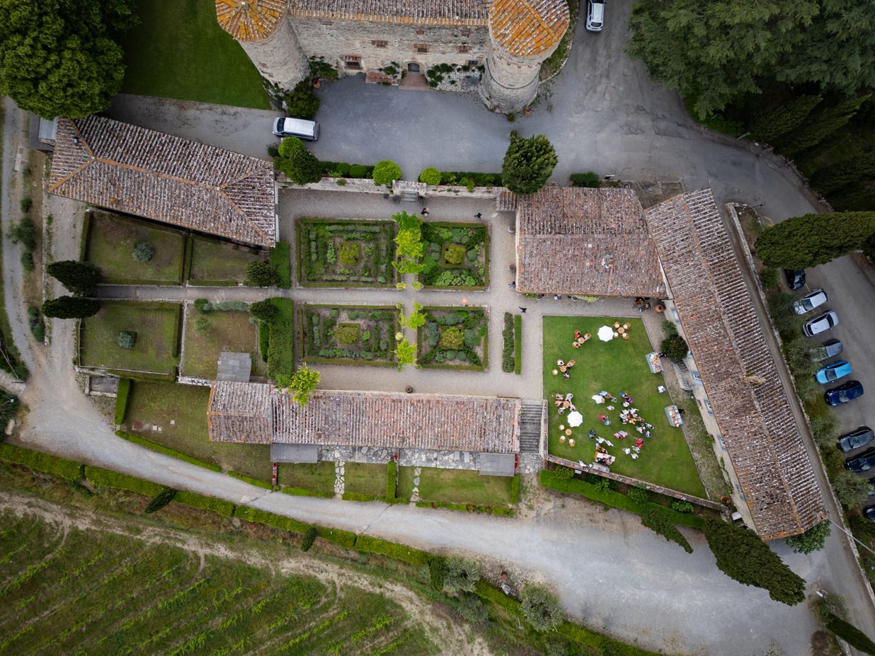 Drone view of the Italian garden at Castello di Meleto during wedding aperitivo, showing guests, garden layout, and the surrounding Chianti landscape in Tuscany.