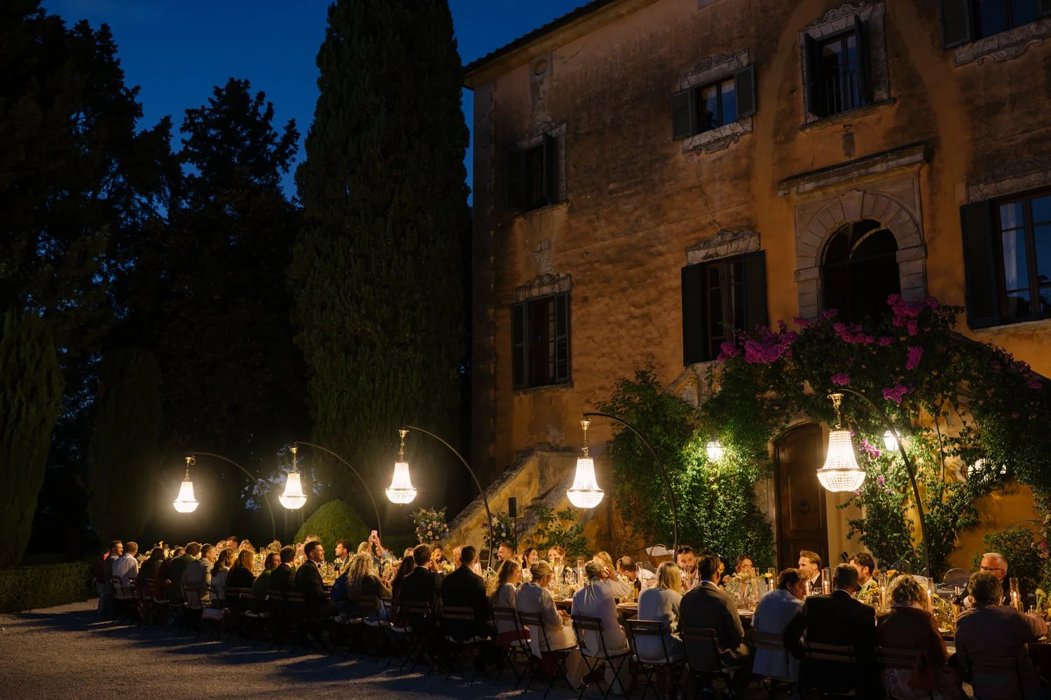 Long-table wedding dinner at night with Villa di Ulignano facade lit behind, October Tuscany wedding photographed by FunkyBird