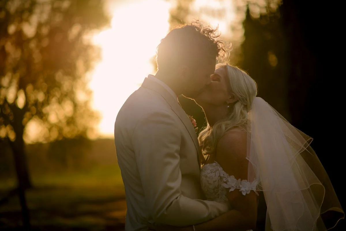 Bride and groom kissing during sunset at Villa Boscarello with warm evening light across the Tuscan landscape.