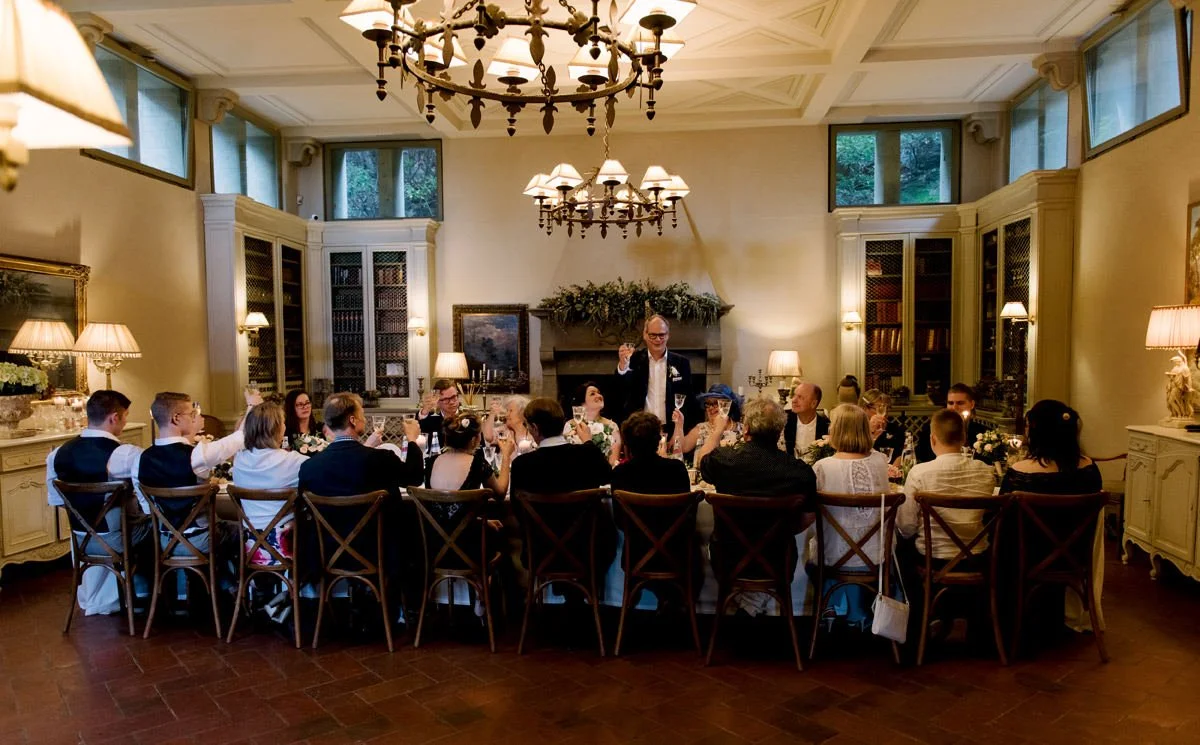 Groom standing and cheering with guests during the wedding dinner inside Villa Le Fontanelle in Florence.