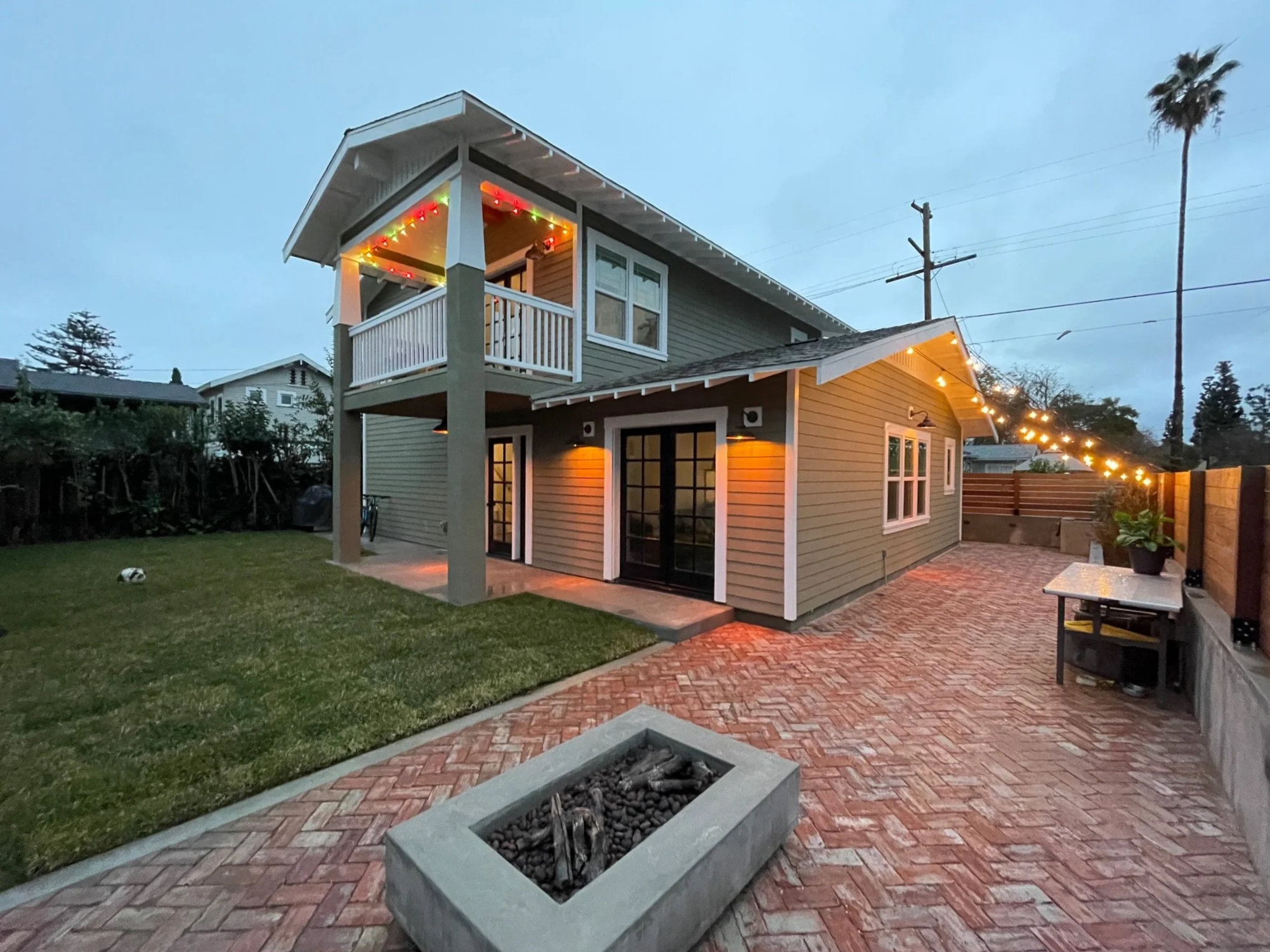 Custom two-story accessory dwelling unit (ADU) in a historic zone in Fullerton, California, featuring craftsman-style architecture, covered balcony, French doors, and warm exterior lighting in a landscaped backyard setting.