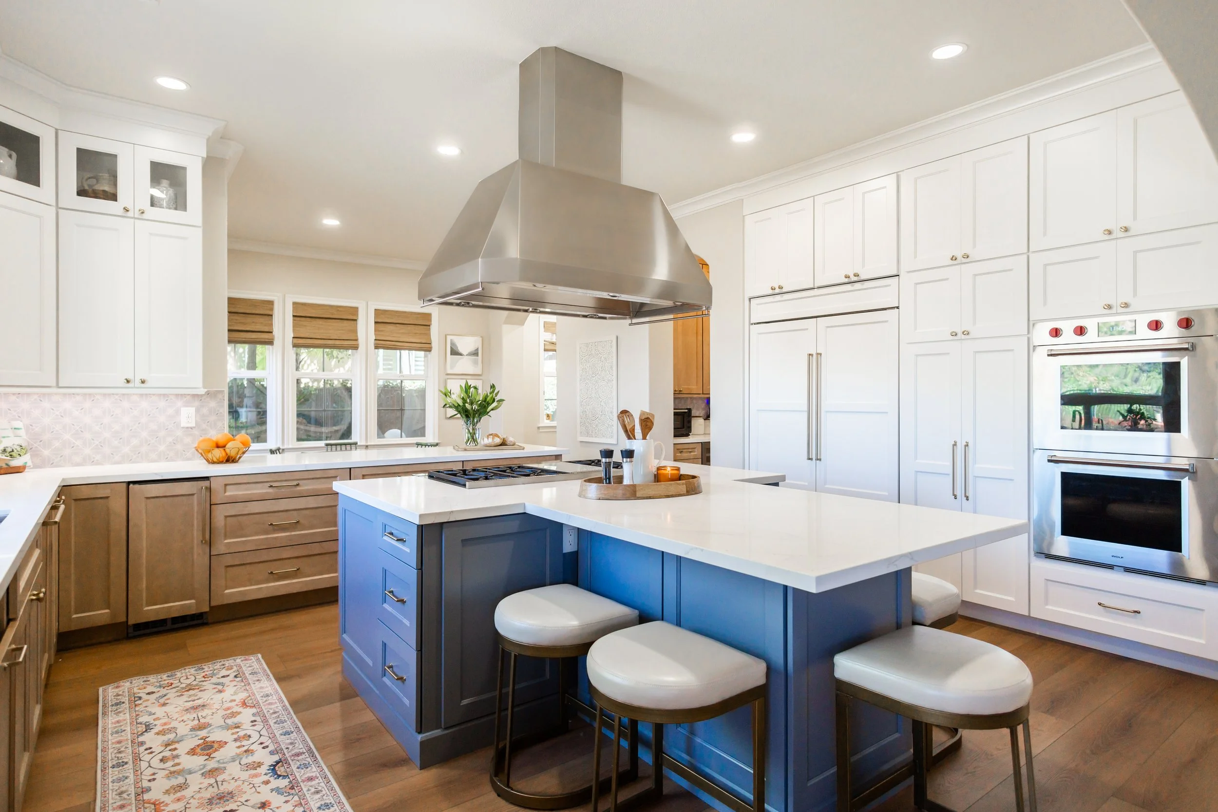 Luxury kitchen remodel in Yorba Linda, California featuring custom white cabinetry, a blue kitchen island, quartz countertops, wide plank wood flooring, stainless steel appliances, and a custom range hood by Apex Construction & Restoration Inc.