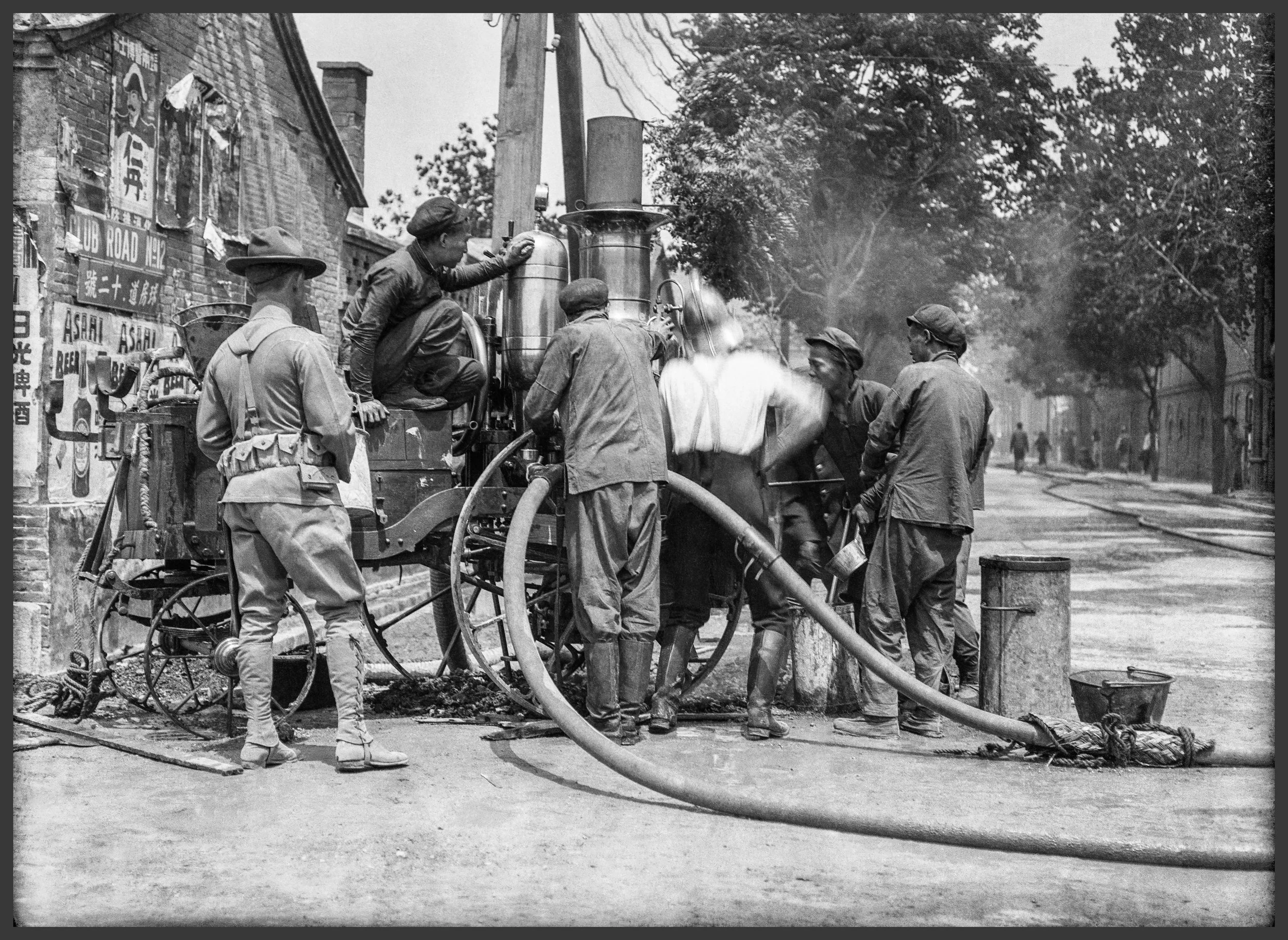 Firemen work to extinguish a fire that seems to be off-frame. A soldier looks on the activity.