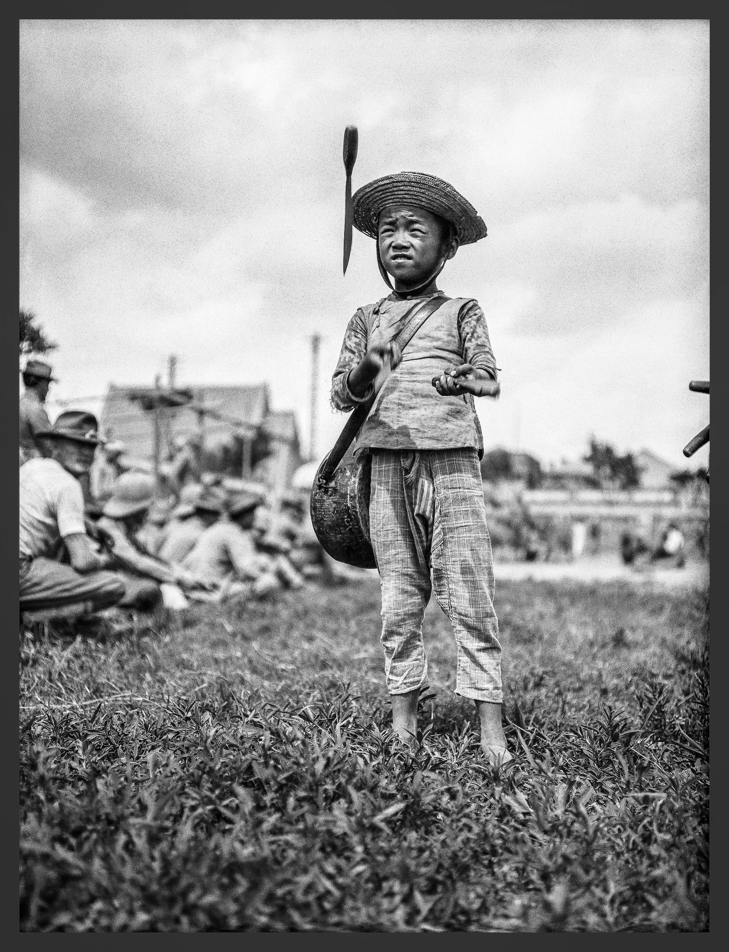 A boy juggles in front of the troops. A calvary solder looks over his shoulder to see the entertainment.
