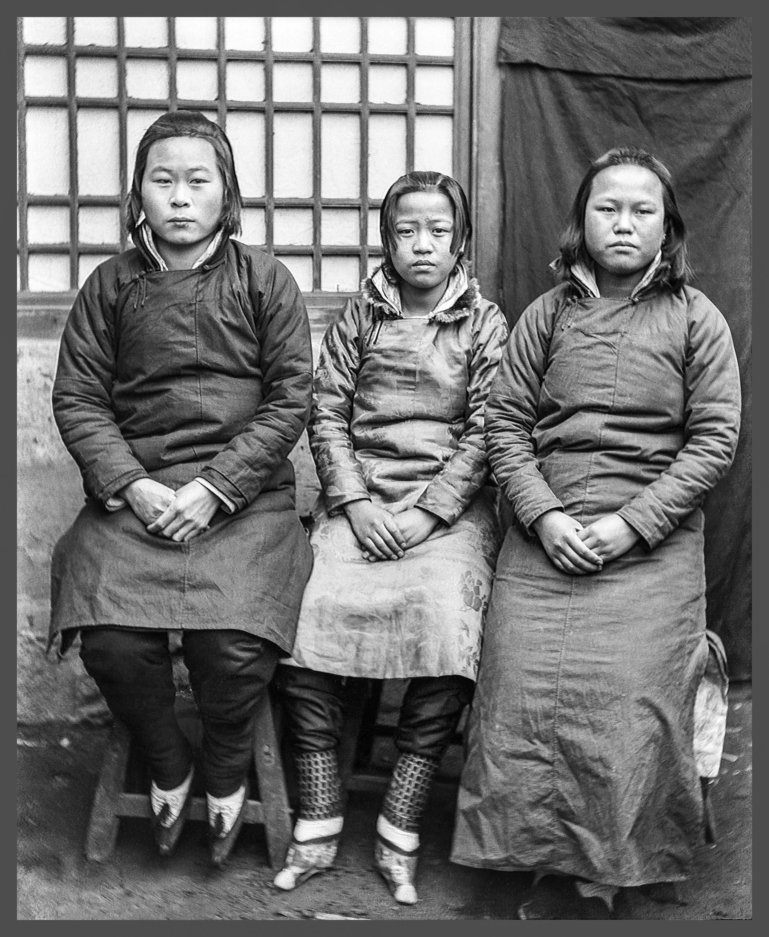 Three young girls sit for a portrait. Foot binding is seen.