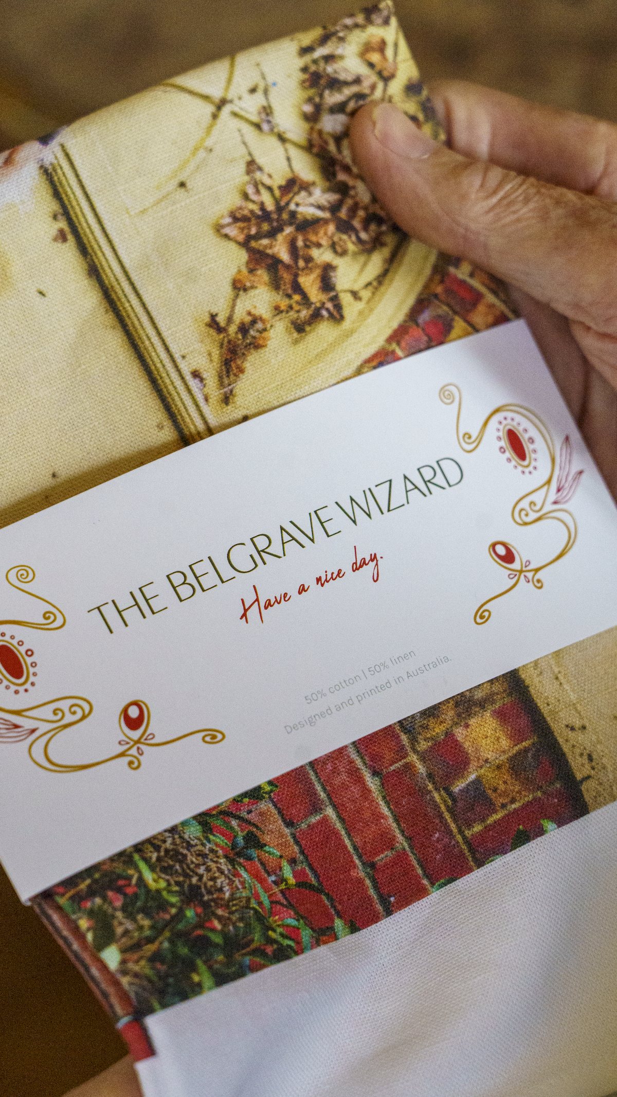 Person holding item labeled 'The Belgrave Wizard' with floral design packaging, 50% cotton and 50% linen, designed and printed in Australia.