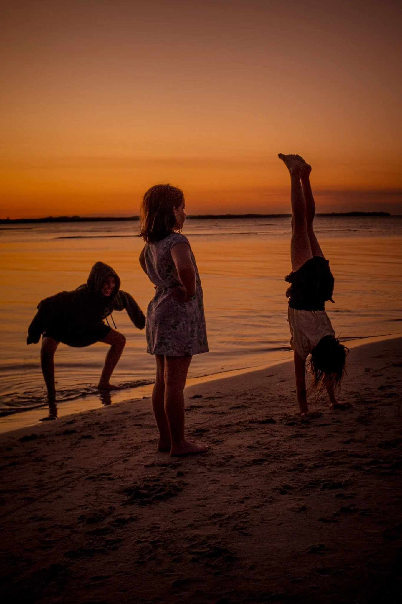 Sunset at Mornington peninsula Capel Sound beach. Three children practice handstands on the edge of the water.