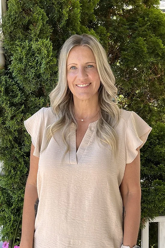 Smiling person with long blonde hair wearing a tan top.