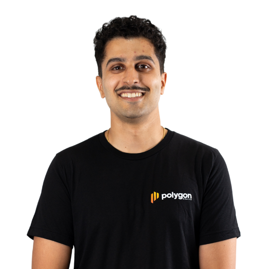 A man with dark curly hair and a mustache wearing a black Polygon t-shirt, smiling at the camera.