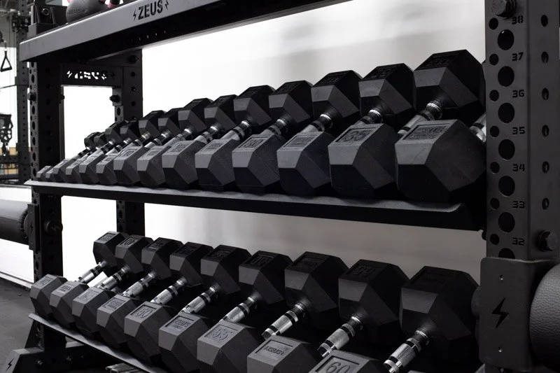 A set of black dumbbells on a multi-tiered black metal rack in a gym.