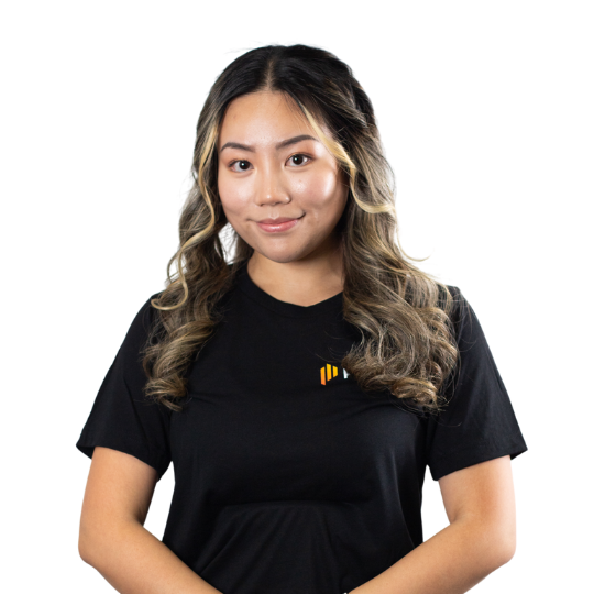 Young woman with long, wavy hair wearing a black t-shirt with a small logo, smiling at the camera.
