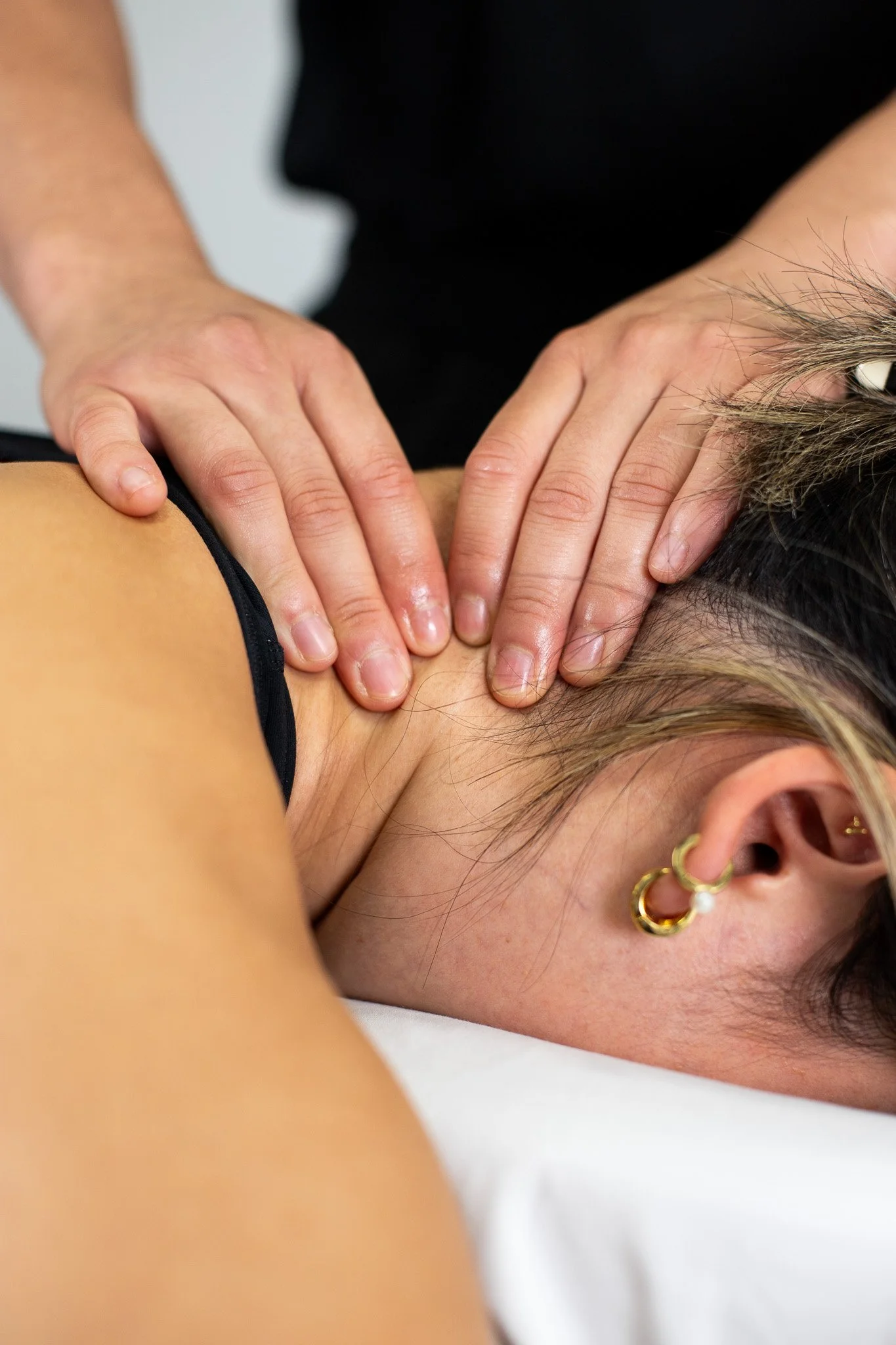 A woman providing physical therapy or injury treatment to a person lying on a table, wearing a black t-shirt with a logo, in a clinical setting.