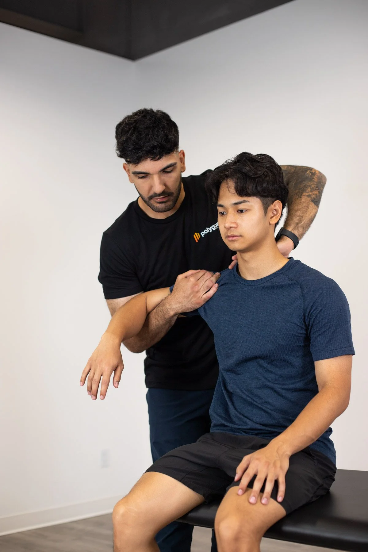 A physical therapist demonstrates shoulder exercises to a young male patient in a clinic.