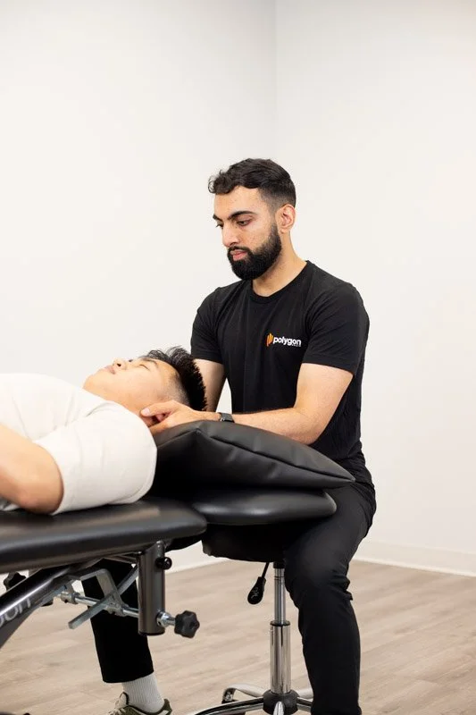 A woman providing physical therapy or injury treatment to a person lying on a table, wearing a black t-shirt with a logo, in a clinical setting.