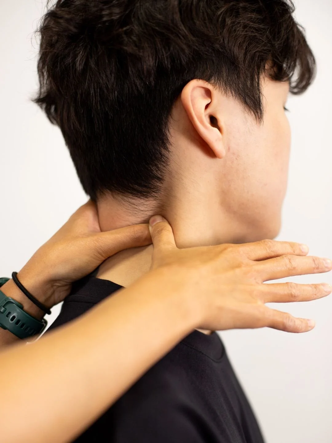 A woman providing physical therapy or injury treatment to a person lying on a table, wearing a black t-shirt with a logo, in a clinical setting.